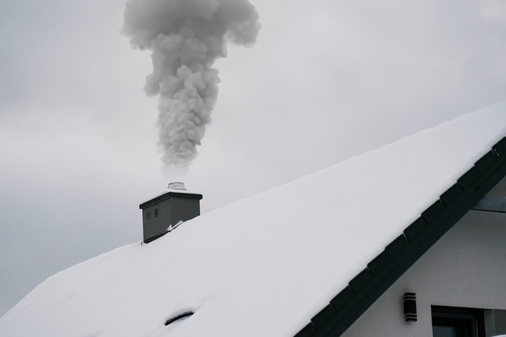 smoke-from-fireplace-warms-up-house-winter-wonderland-as-snow-falls-covers-roof-surrounding-trees