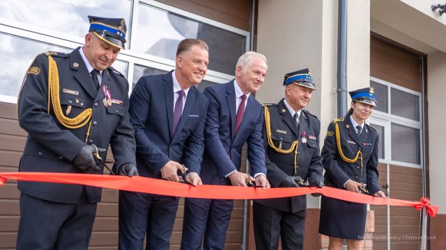 Czterech mężczyzn, w tym trzej oficerowie straży pożarnej, przecina czerwoną wstęgę, symbolizując otwarcie nowej komendy w Pucku.