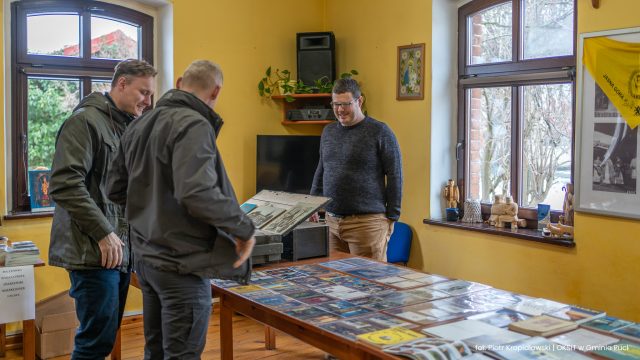 Zdjęcie przedstawia kolekcjonera z mieszkańcami oglądających wystawę